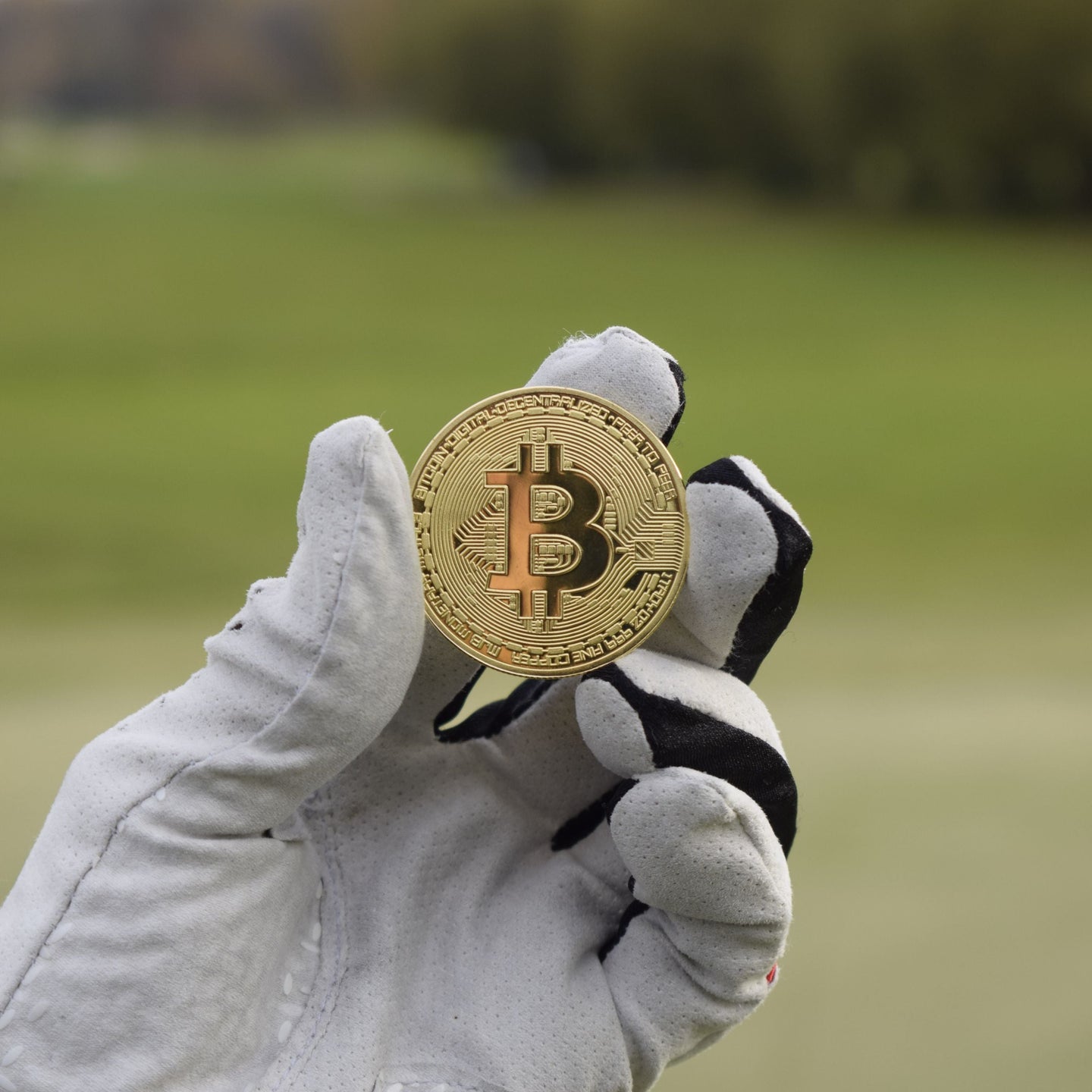 En person med golfhandske som håller i en bitcoin ballmarker