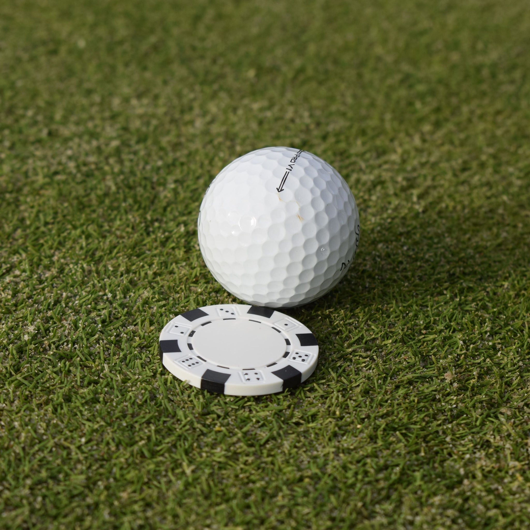 Närbild på den vita markören som följer med när du köper Poker ballmarker som ligger på en greenn bakom en golfboll.