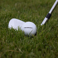 Närbild på en Vice Pro Plus golfboll i gräset framför en golfklubba.