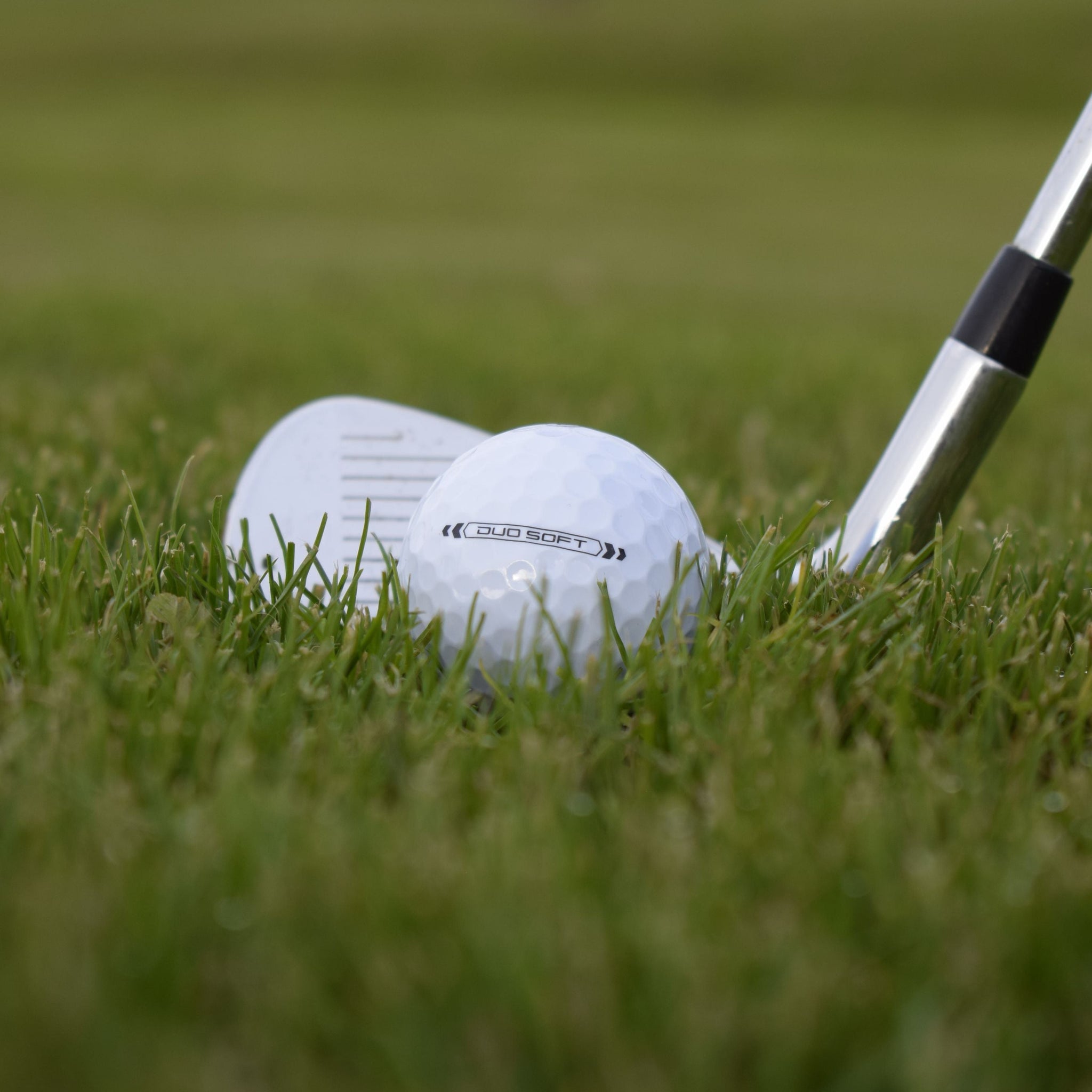 En närbild på Wilson Duo Soft som ligger i gräset framför en golfklubba.