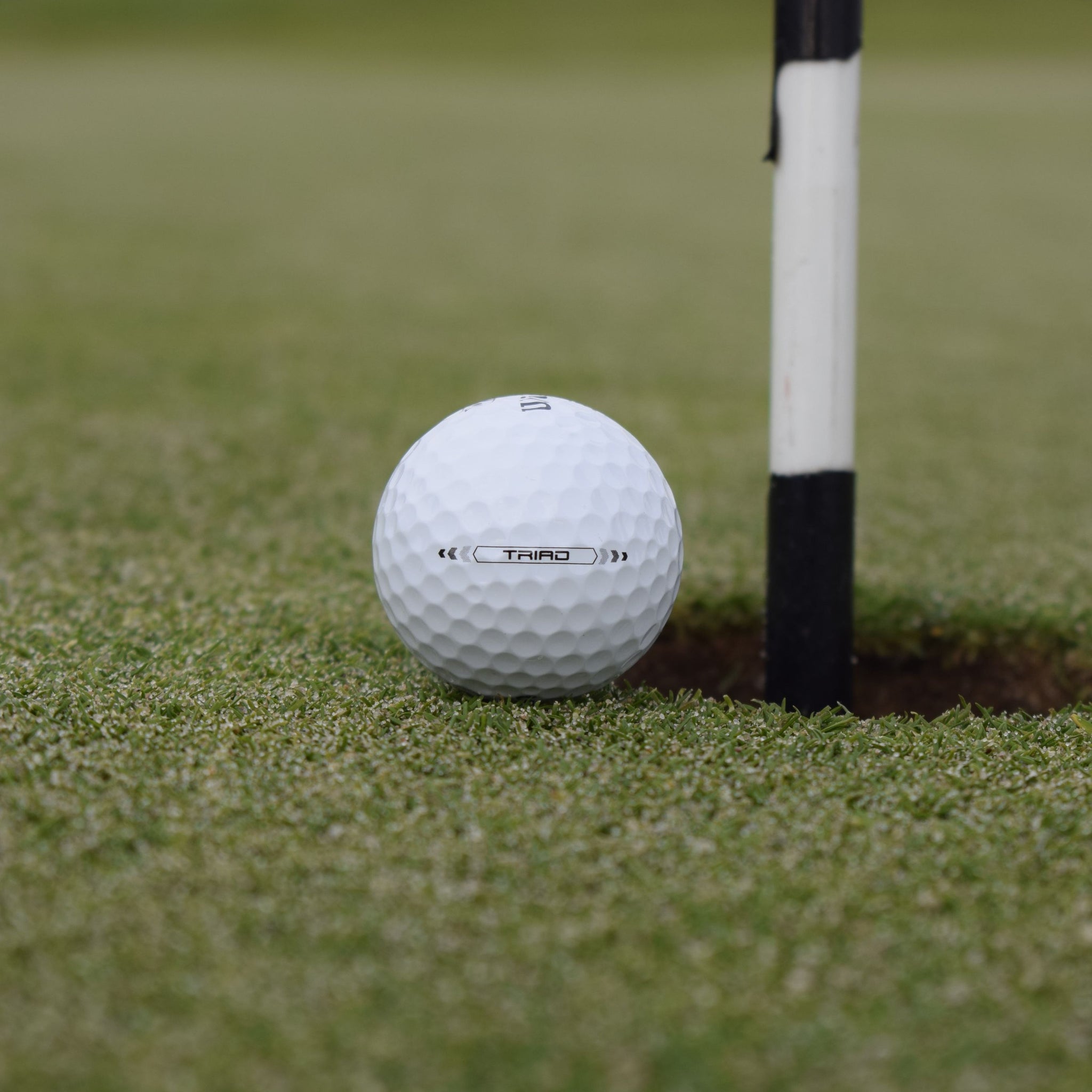 En Närbild på Wilson Staff Triad golfboll som ligger precis vid hålet på en golfbana.